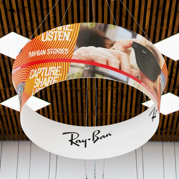 Curved banner displaying Ray-Ban Stories smart glasses ad, suspended in a room with striped walls, emphasizing 'Listen. Capture. Share.'